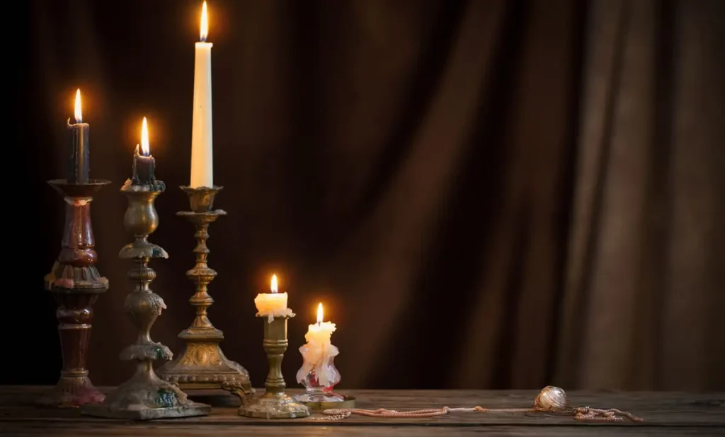 Antique candlestick with a lit candle on an old wooden table against a brown velvet curtain