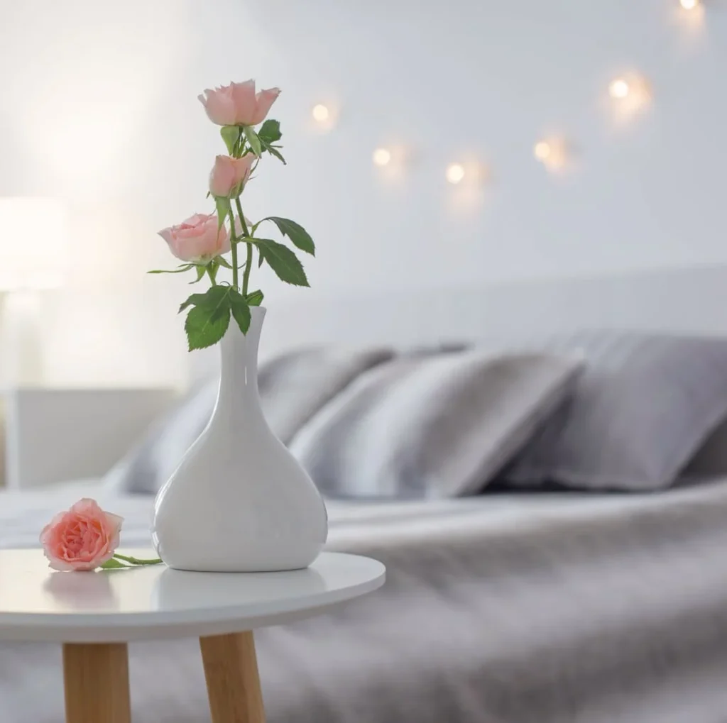 Blush pink roses in a vase on a bedroom table, showing a pink and cream color palette