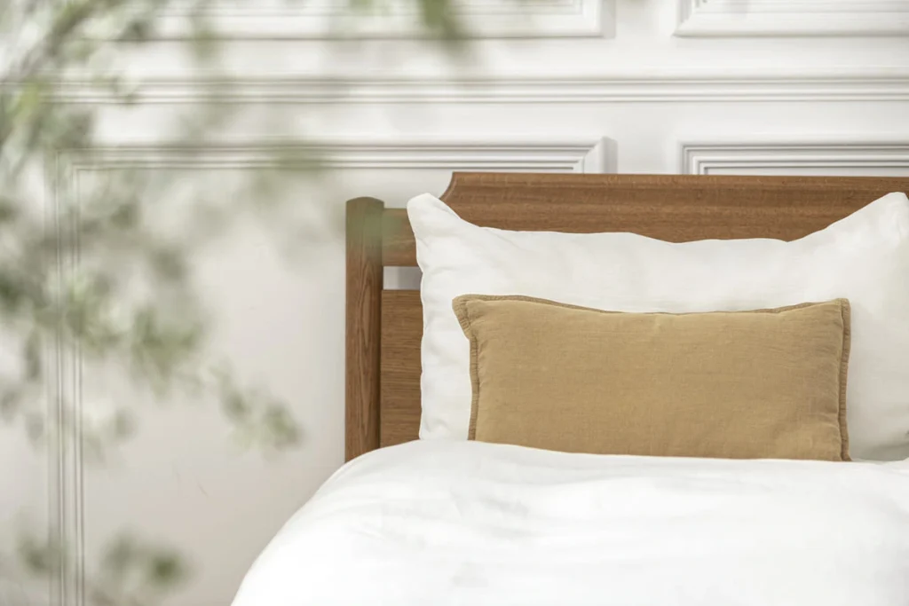 Clean girl room color palette with a beige linen cushion on warm white bedding