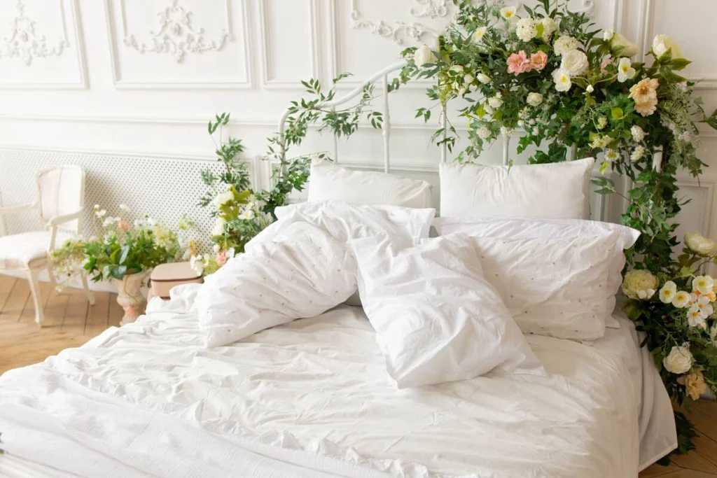 Coquette room decor on the bed: white linens, white pillows and a headboard decorated with flowers