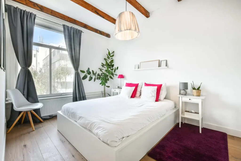 White bedroom with pink pillows, a green plant and wooden ceiling beams, a grown-up take on a themed room