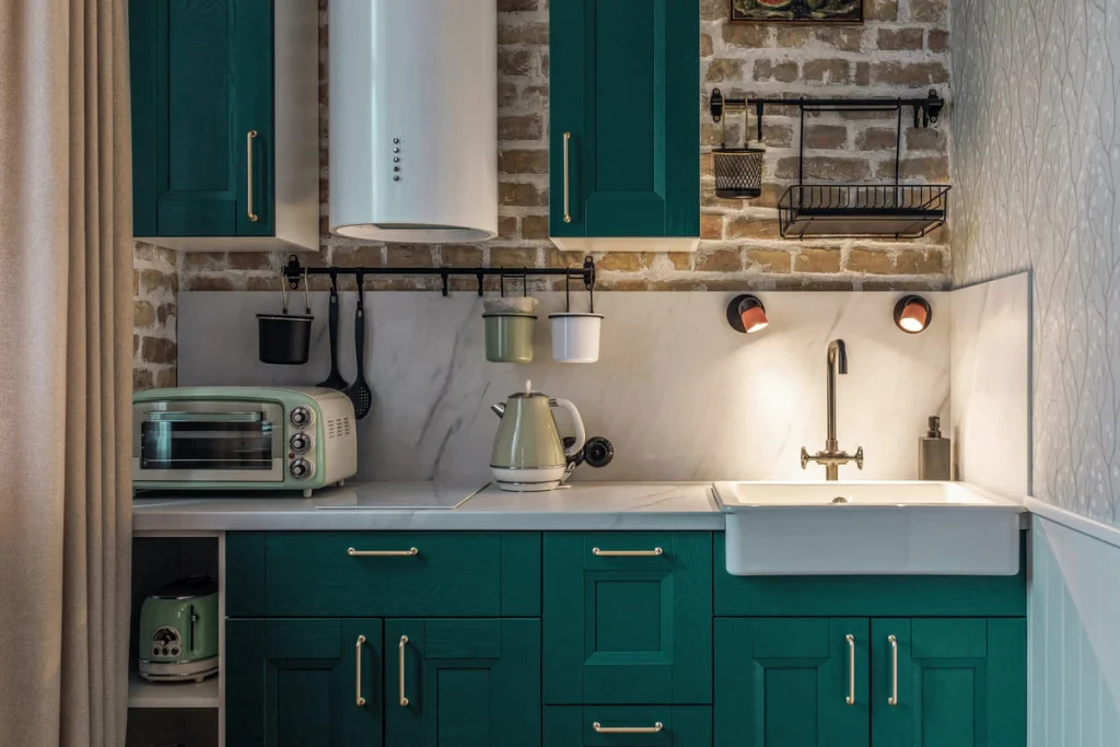 Dark green kitchen cabinets against an exposed brick wall