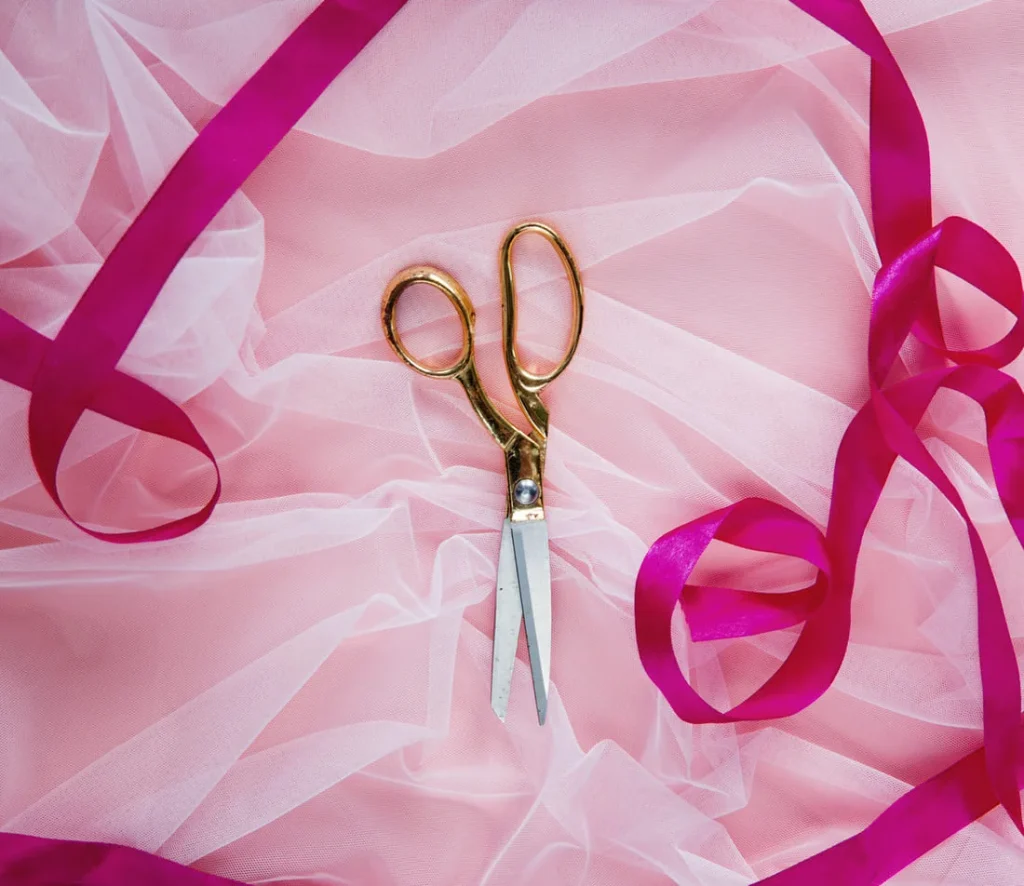 Gold scissors and satin ribbon on pink tulle, ready for making DIY bows