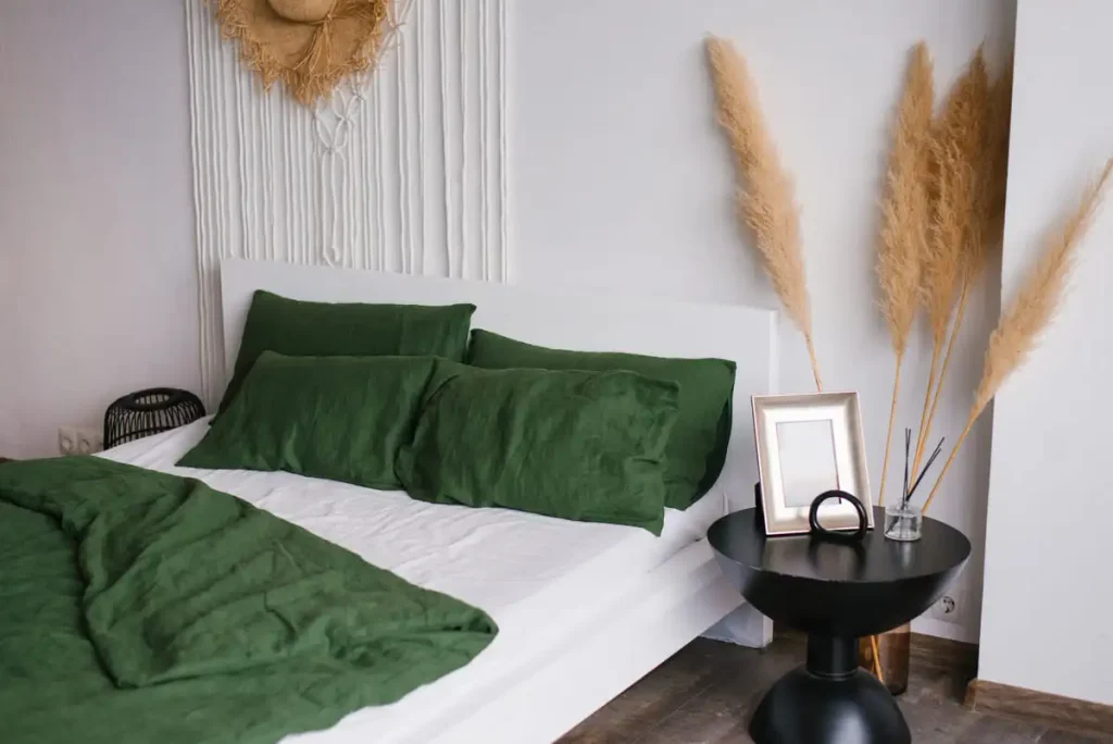 Rustic bedroom with white and green bed linen and dried flowers beside the bed
