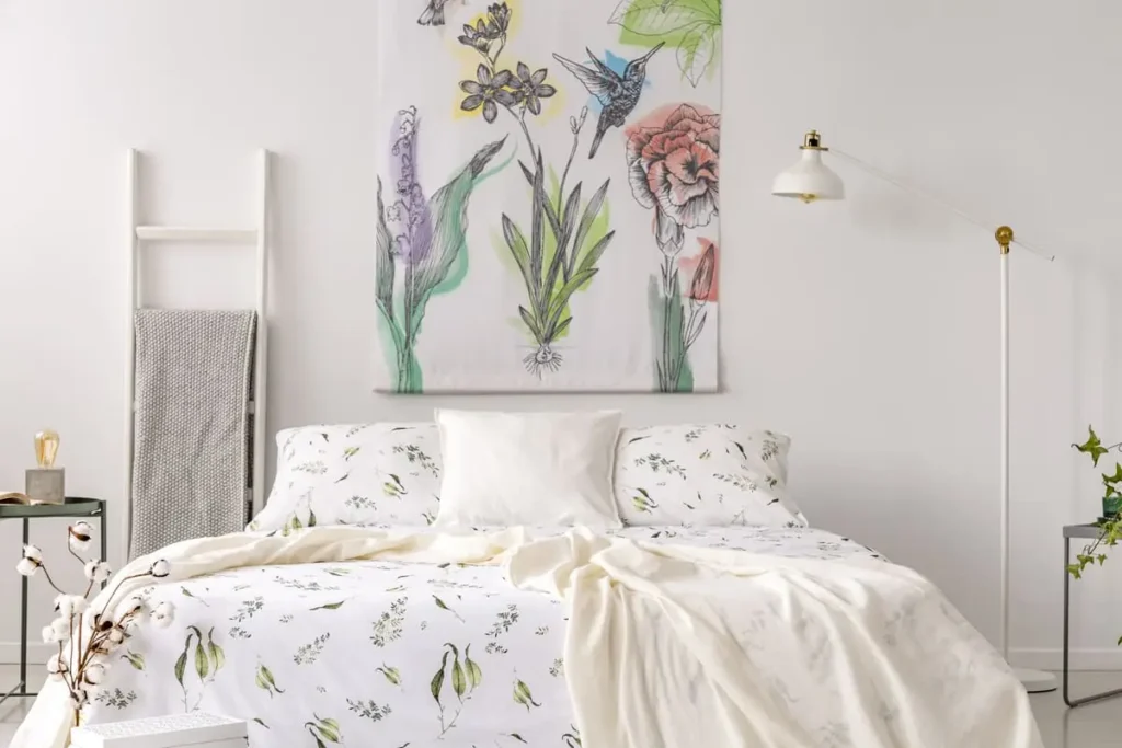 Fairycore bedroom with white bedding in a green leaf print and a flower-and-bird painted fabric behind the bed