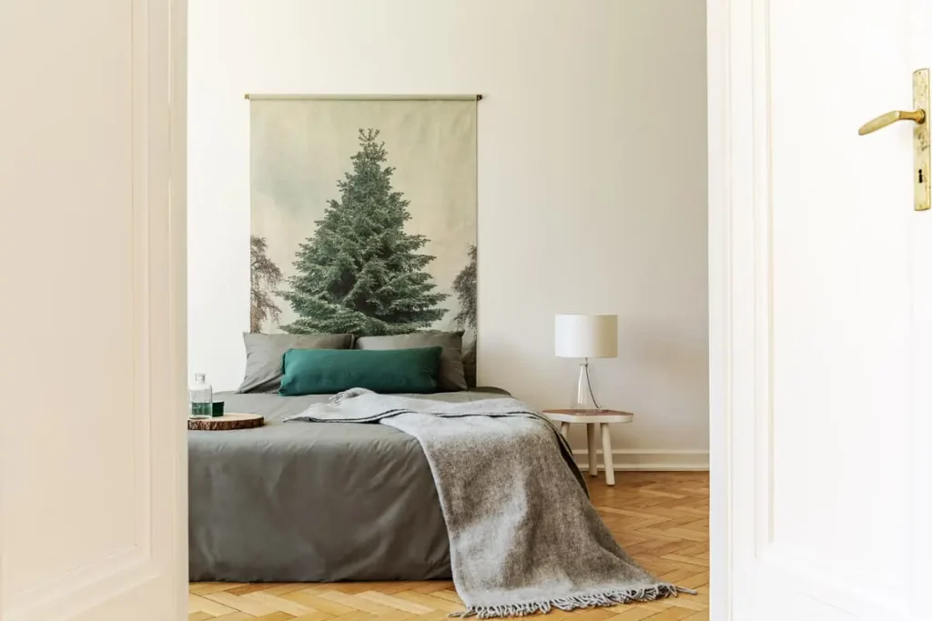 Simple bedroom with gray and green bedding, a wool throw and an evergreen tree print on the wall
