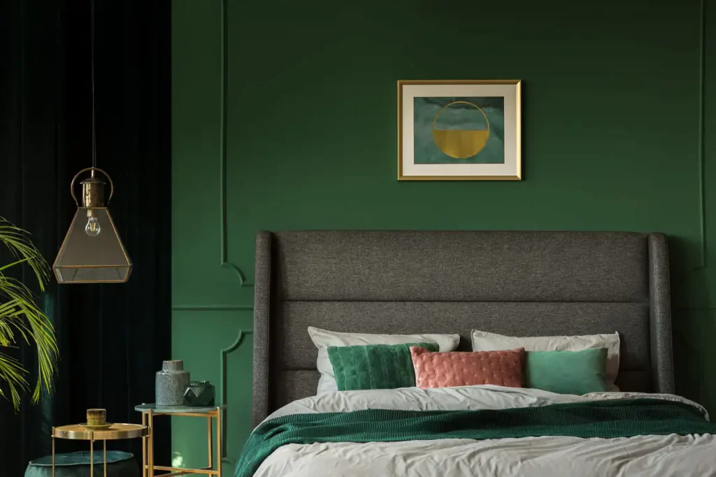 Dark green painted wall behind a bed with a framed poster, a simple start for a dark cottagecore bedroom