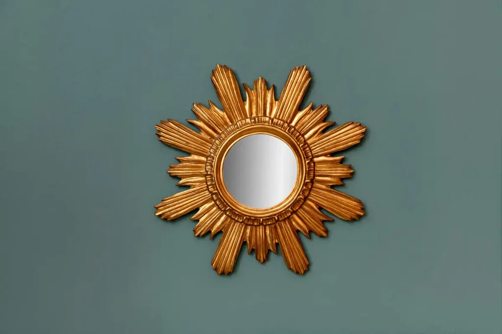 Round mirror with a gilded starburst frame hanging on a teal wall