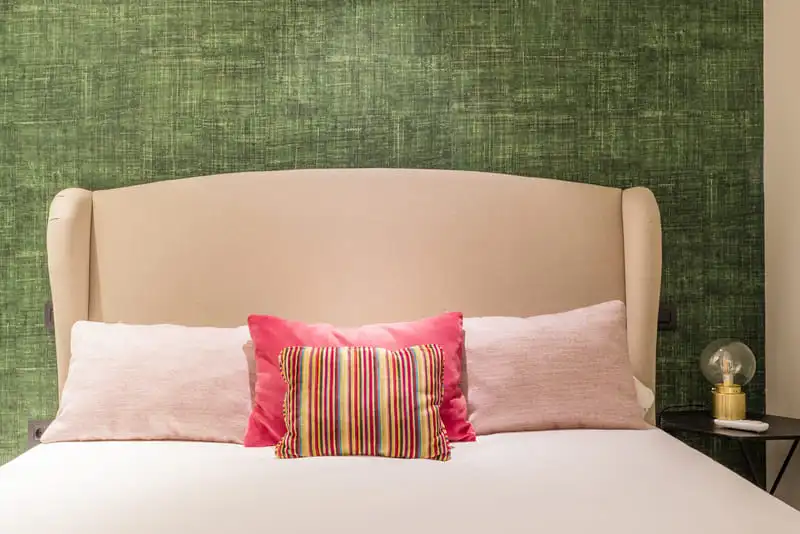 Green patterned wallpaper behind an upholstered headboard with pink and red cushions