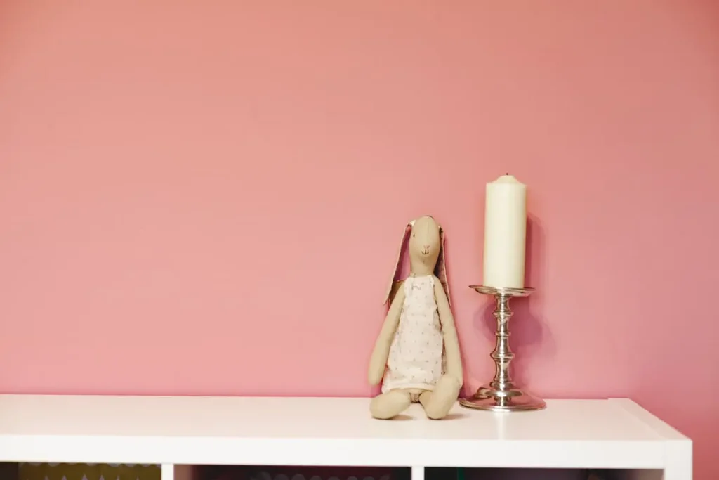 Plush bunny and a candle on a white shelf against a pink wall, a simple display idea for hello kitty room ideas