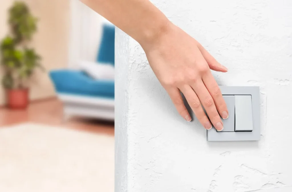 Hand pressing a wall light switch, which has to stay on for smart bulbs to respond