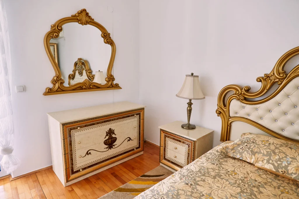 Ornate carved-frame mirror hung on the wall above a chest of drawers in a bedroom