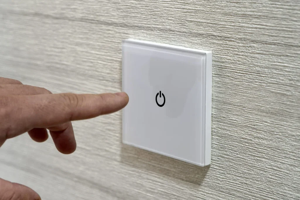 Finger pressing a modern touch light switch on a white wall