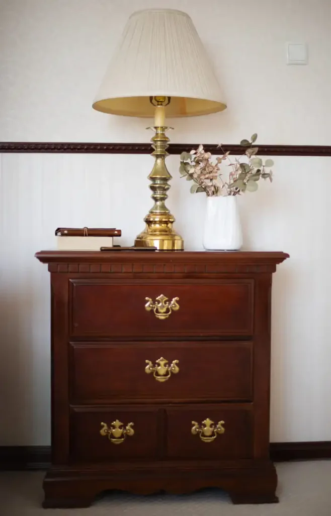 Vintage nightstand with a brass lamp and books in a Nancy Meyers bedroom